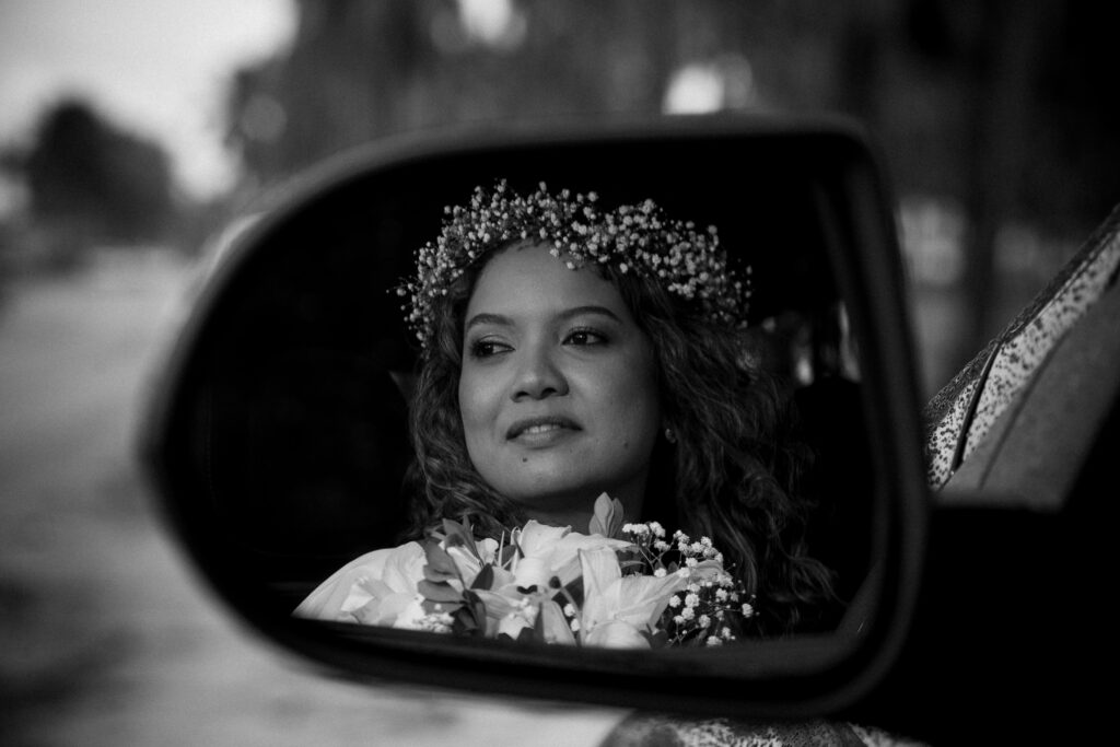 Black and white portrait of a bride seen in a car mirror, capturing her serene expression and floral wreath.